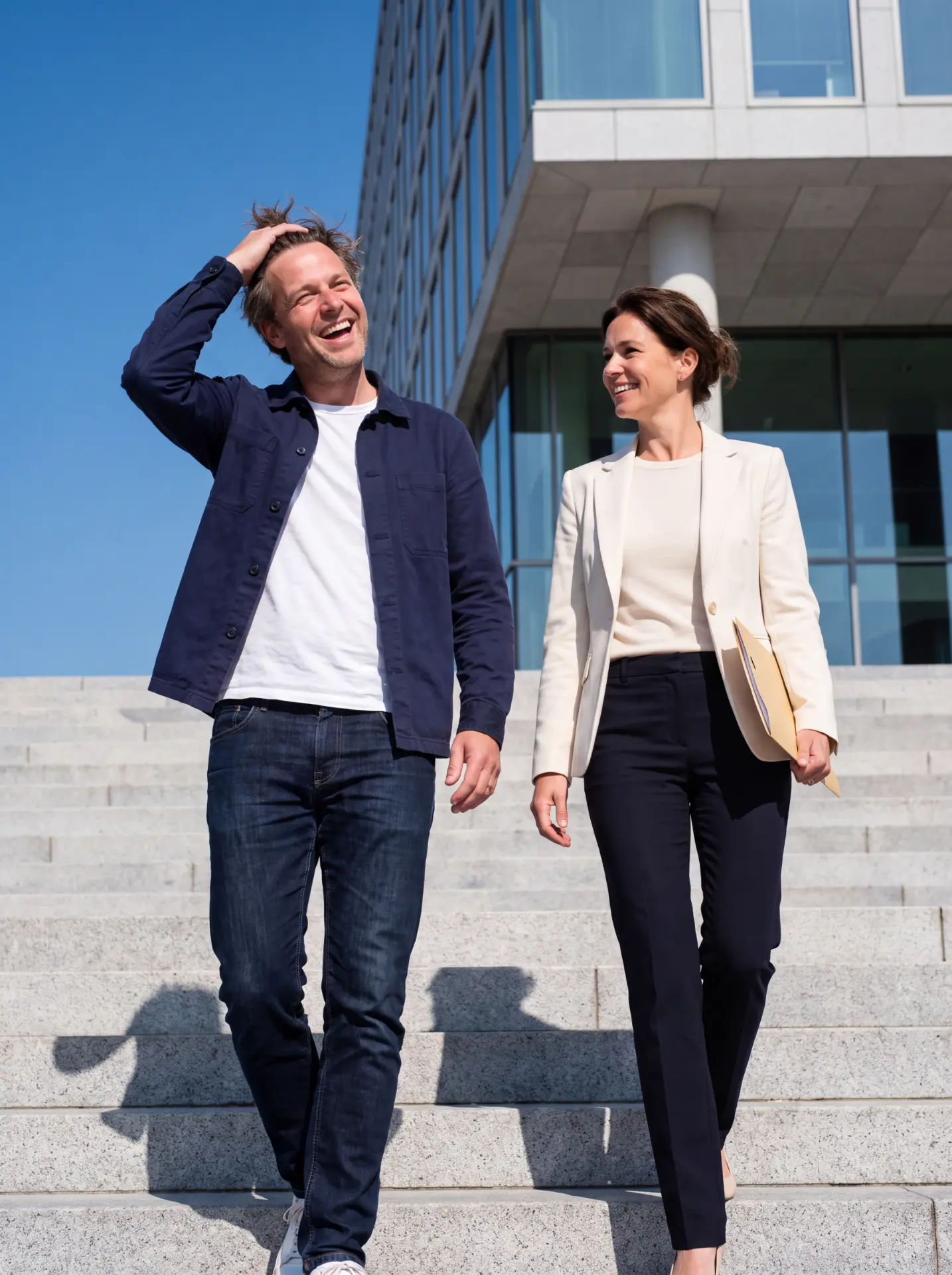 Twee ondernemers lachen terwijl ze van een kantoorpand naar beneden lopen.